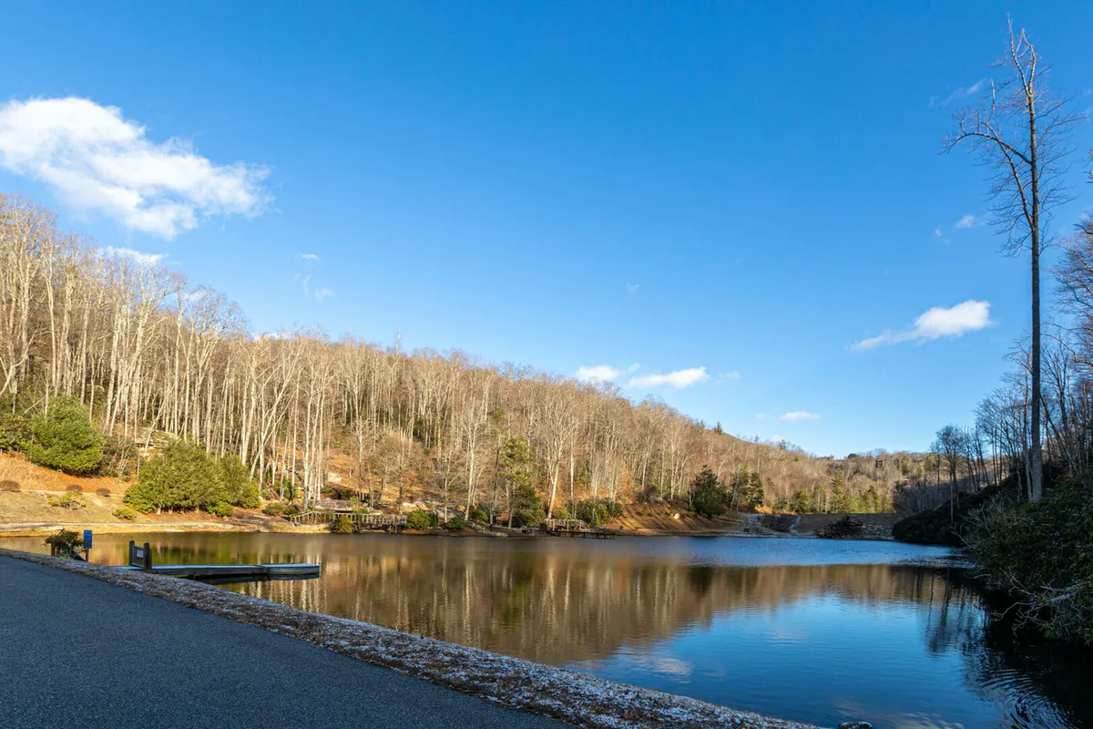 A peaceful lake bordered by trees and rolling hills, with a wooden pier extending over the calm water. The setting invites activities like fishing, canoeing, picnicking, and bird watching, tying into the riverside and lake amenities described in the section.