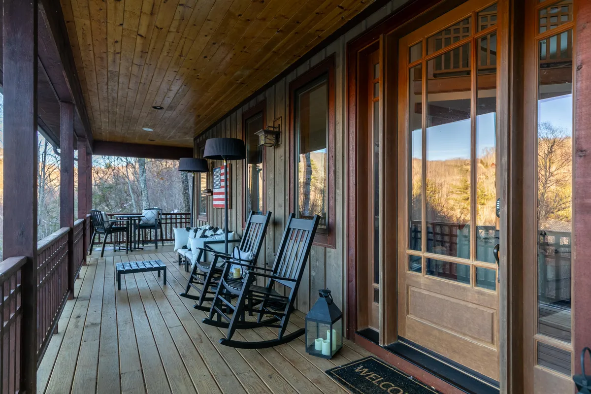 A welcoming exterior porch with rocking chairs, lantern, and front door, complemented by a table and chairs arrangement. The inviting atmosphere encourages moments of relaxation, conversation, and connection with nature.
