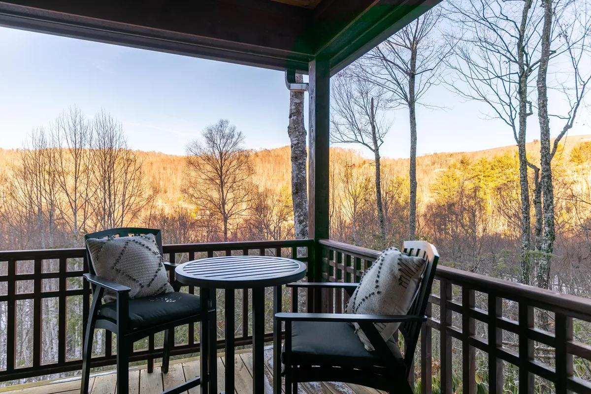 A welcoming balcony setting with comfortable seating and a table, all oriented toward sweeping mountain vistas. The scene is serene, perfect for enjoying morning coffee or unwinding while watching the sun set or the stars come out. The relaxed arrangement of the chairs and the open sky evoke a sense of openness and tranquility.