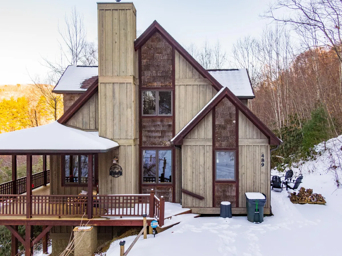 The image showcases a charming wooden mountain home nestled in a tranquil, snow-covered landscape. The house features a spacious deck and expansive windows, inviting natural light and offering breathtaking winter views. The serene setting hints at cozy indoor moments and outdoor relaxation, perfect for both adventure and unwinding.