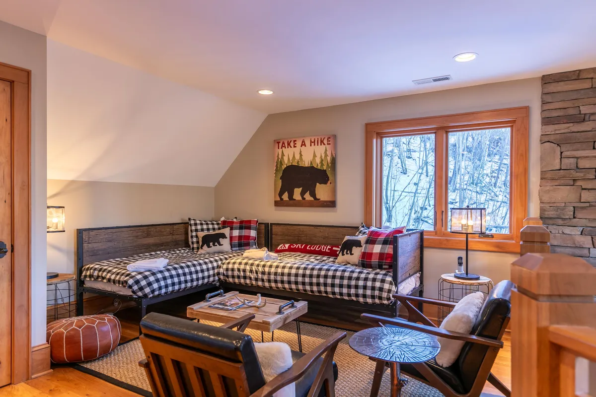 A charming loft area featuring twin bunk beds, rustic wooden furniture, colorful wall art, and large windows that fill the space with light. The setting is playful yet restful, ideal for families or groups of friends seeking flexible sleeping arrangements.