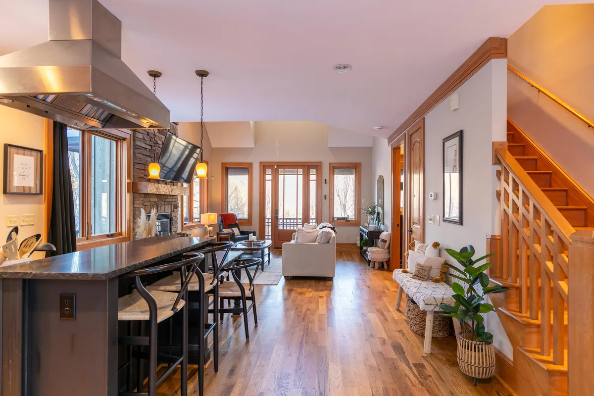 A cozy living area featuring a kitchen island, a warm fireplace, comfortable seating, and expansive windows that frame outdoor views. The mood is inviting, suggesting relaxation after outdoor adventures or gathering for warm drinks during colder months.