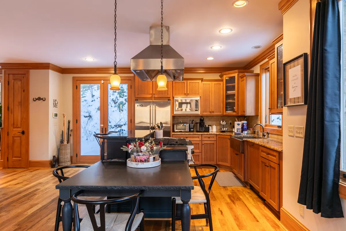 A gourmet kitchen featuring a central island with seating, stainless steel appliances, and large windows overlooking a snowy landscape. The space feels bright, modern, and inviting for meal preparation and social gatherings.