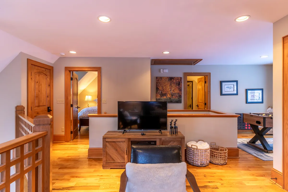 A cozy interior scene showing a television, wooden furniture, artwork on the wall, a foosball table, and baskets with towels. The space is arranged to welcome both game nights and movie marathons, embodying a comfortable family-friendly zone.